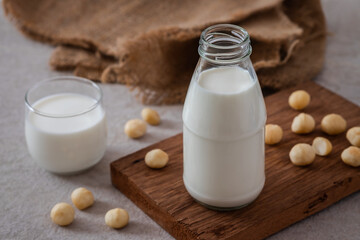 Bottle of macadamia milk on wooden board and macadamia milk in glass.