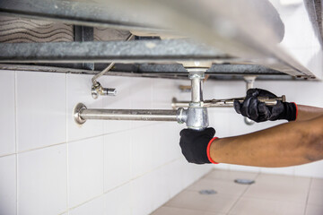 Technician plumber using a wrench to repair a water pipe under the sink. Concept of maintenance,...