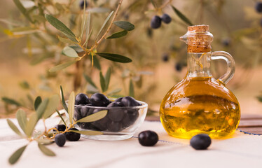 olive oil in a glass bottle and green olives on the background of olive branches in the garden