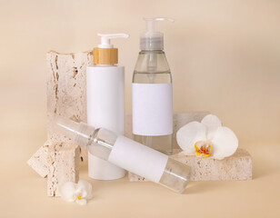 Cosmetic bottles near white orchid flowers and stones on light beige, package Mockup