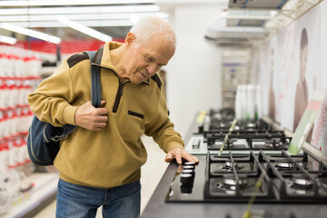 senor man pensioner buying kitchen stove in showroom of electrical appliance store