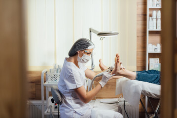 Podologist foot doctor in mask on face, making procedure for foot with special equipment - obrazy, fototapety, plakaty