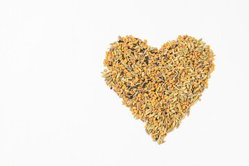 Heart shaped panch phoron or panch foran conventional Indian mixture of spicy seeds for cooking withf fenugreek, fennel, cumin, zira isolated on white with copy space.