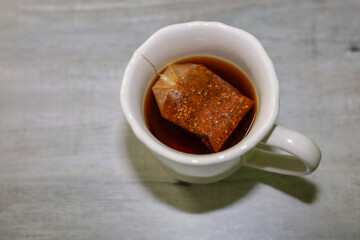 Top view of a rooibos tea bag steeping in a cup of hot water.