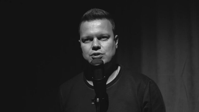 a man speaks into a microphone in a dark recording studio. black and white version.