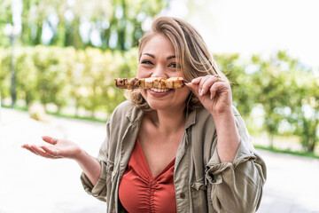 Young chubby woman having fun in the parkland at barbecue making faces holding skewers