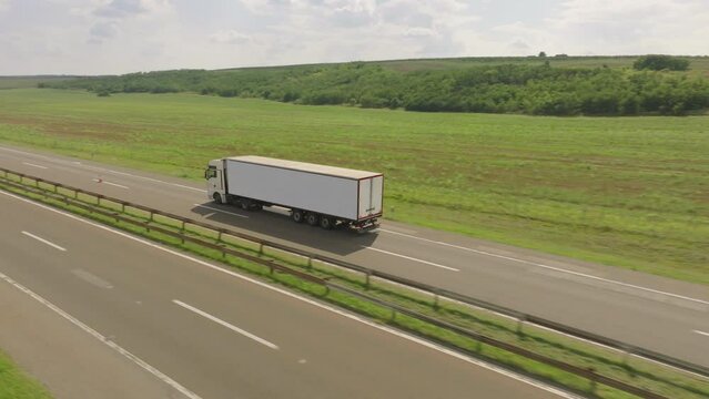 Aerial shot of a fast truck on the road in beautiful countryside with green grass in the summer