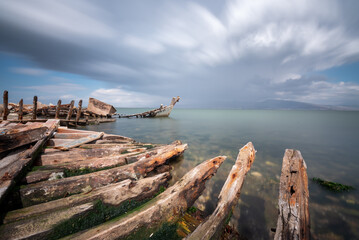 Long exposure photography, sunken boat on blue sea with a city view on background moving clouds blurry concept