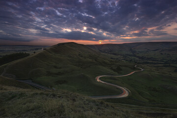 View towards Lords Seat from Mam Tor with car light trails at Sunset. Peak District, Derbyshire