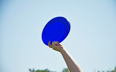 Woman's hand with a manicure holds a blue frisbee against the sky