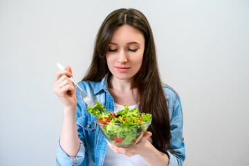 Beautiful young woman eats salad with lettuce, tomato and olives