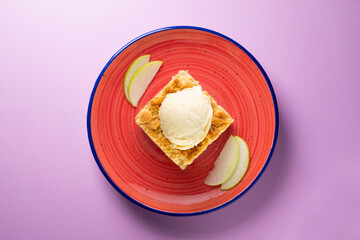 Apple crumble with vanilla ice cream on a red ceramic plate.