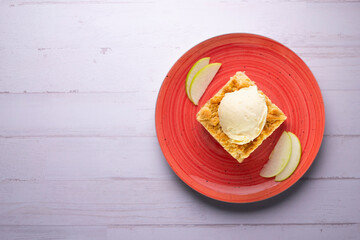 Apple crumble with vanilla ice cream on a red ceramic plate.