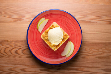 Apple crumble with vanilla ice cream on a red ceramic plate.