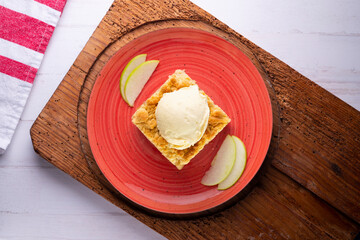 Apple crumble with vanilla ice cream on a red ceramic plate.