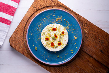 Yogurt and pistachio mousse decorated with red flowers on a blue ceramic plate. Traditional French recipe.