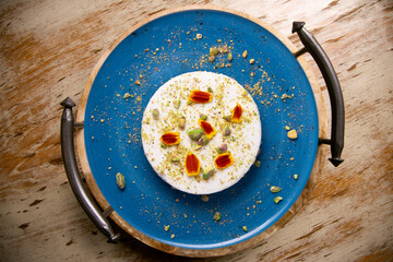 Yogurt and pistachio mousse decorated with red flowers on a blue ceramic plate. Traditional French recipe.