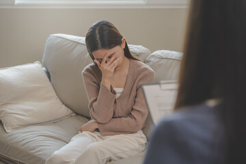 Fototapeta premium Psychology, sad asian young woman, girl cover face with hand, consulting with psychologist, psychiatrist while patient counseling mental with doctor woman taking notes at clinic. Encouraging, therapy.