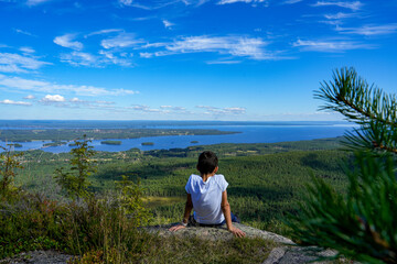 Naklejka na ściany i meble Kind schaut auf dem Berg in die Natur mit Seenlandschaft in Schweden Skandinavien mit blauem Himmel im Hintergrund und viel Wasser