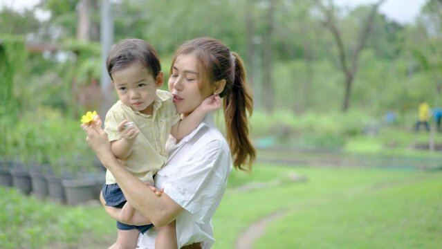 Happy mother spending time with son and mom kisses her baby at park, Cheerful adult mommy playing with cute funny kid baby having fun together, Soft touch, love care