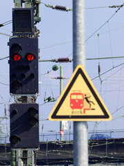 Red signal at the train station with a warning sign.