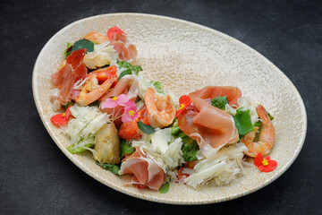 Salad with shrimps, cheese and prosciutto, on a plate