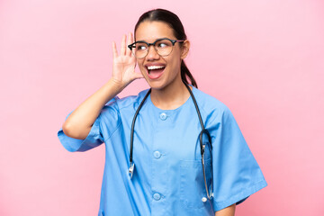 Young nurse Colombian woman isolated on pink background listening to something by putting hand on the ear