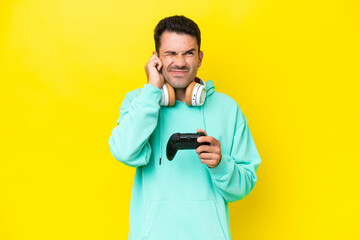 Young handsome man playing with a video game controller over isolated wall frustrated and covering ears © luismolinero