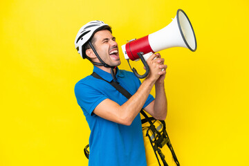 Young handsome man with thermal backpack over isolated yellow background shouting through a megaphone