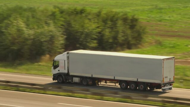 Aerial video of a cargo truck riding fast on the highway road through agricultural field in countryside
