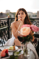 A beautiful young woman wrapped in a white blanket is having dinner on the balcony at a table.