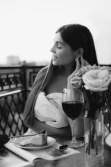 A beautiful young woman wrapped in a white blanket is having dinner on the balcony at a table. Black and white image. 