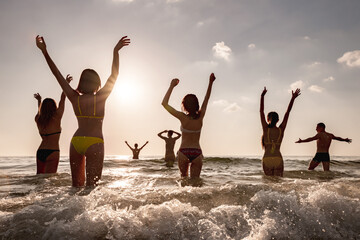 Group of happy young friends are relaxing at sunset sea beach. Tropical vacations concept
