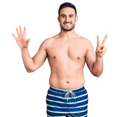 Fototapeta premium Young handsome man wearing swimwear showing and pointing up with fingers number seven while smiling confident and happy.