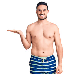 Fototapeta na wymiar Young handsome man wearing swimwear smiling cheerful presenting and pointing with palm of hand looking at the camera.