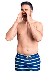 Fototapeta premium Young handsome man wearing swimwear shouting angry out loud with hands over mouth