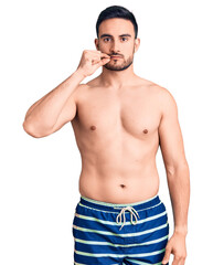 Young handsome man wearing swimwear mouth and lips shut as zip with fingers. secret and silent,...