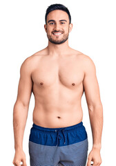 Fototapeta premium Young handsome man wearing swimwear looking positive and happy standing and smiling with a confident smile showing teeth