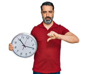 Middle aged man with beard holding big clock with angry face, negative sign showing dislike with thumbs down, rejection concept