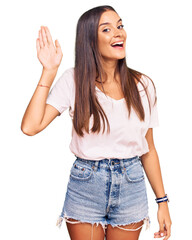 Young hispanic woman wearing casual white tshirt waiving saying hello happy and smiling, friendly welcome gesture © Krakenimages.com