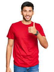 Young handsome man wearing casual red tshirt doing happy thumbs up gesture with hand. approving...