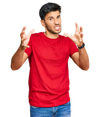Fototapeta premium Young handsome man wearing casual red tshirt shouting frustrated with rage, hands trying to strangle, yelling mad