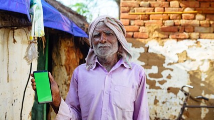 Old Asian man smiling and showing a green screen cell phone with rural village life concept background.