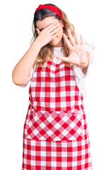 Young caucasian woman wearing apron covering eyes with hands and doing stop gesture with sad and fear expression. embarrassed and negative concept.