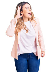 Young caucasian woman wearing business clothes smiling with hand over ear listening an hearing to rumor or gossip. deafness concept.