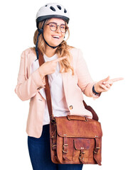 Young caucasian woman wearing bike helmet and leather bag smiling and looking at the camera pointing with two hands and fingers to the side.
