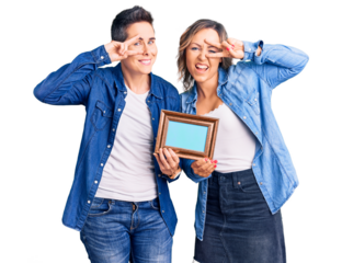 Couple of women holding empty frame doing peace symbol with fingers over face, smiling cheerful showing victory