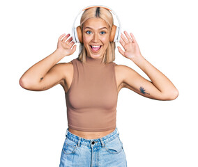 Beautiful young blonde woman listening to music using headphones celebrating crazy and amazed for...
