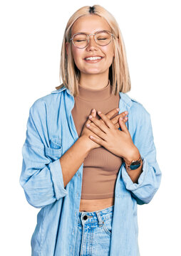 Beautiful young blonde woman wearing glasses smiling with hands on chest with closed eyes and grateful gesture on face. health concept.
