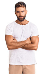 Young hispanic man wearing casual white tshirt skeptic and nervous, disapproving expression on face with crossed arms. negative person.